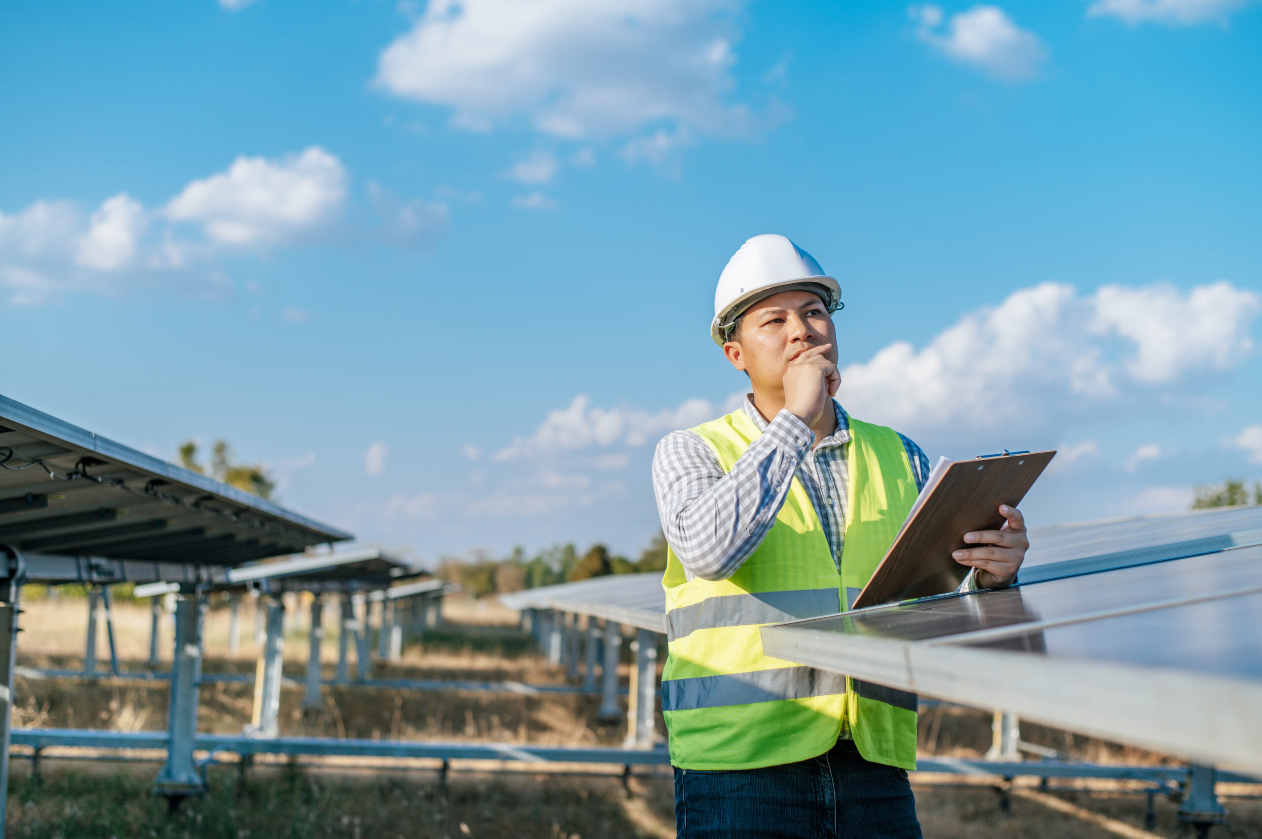Young Asian Inspector Engineer man working at solar farm, Technician or supervisor male in white helmet Checking operation of sun and photovoltaic solar panel in station, copy space